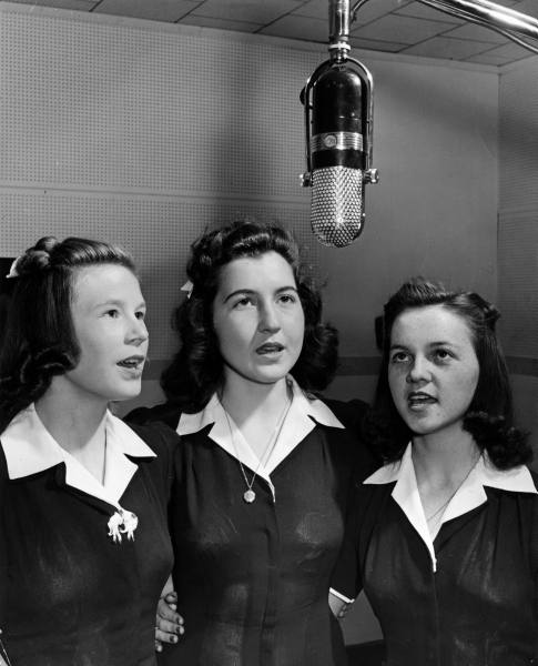 Vokalist_studio_Trio of high school girls singing in harmony beneath microphone in studio of loc.jpg